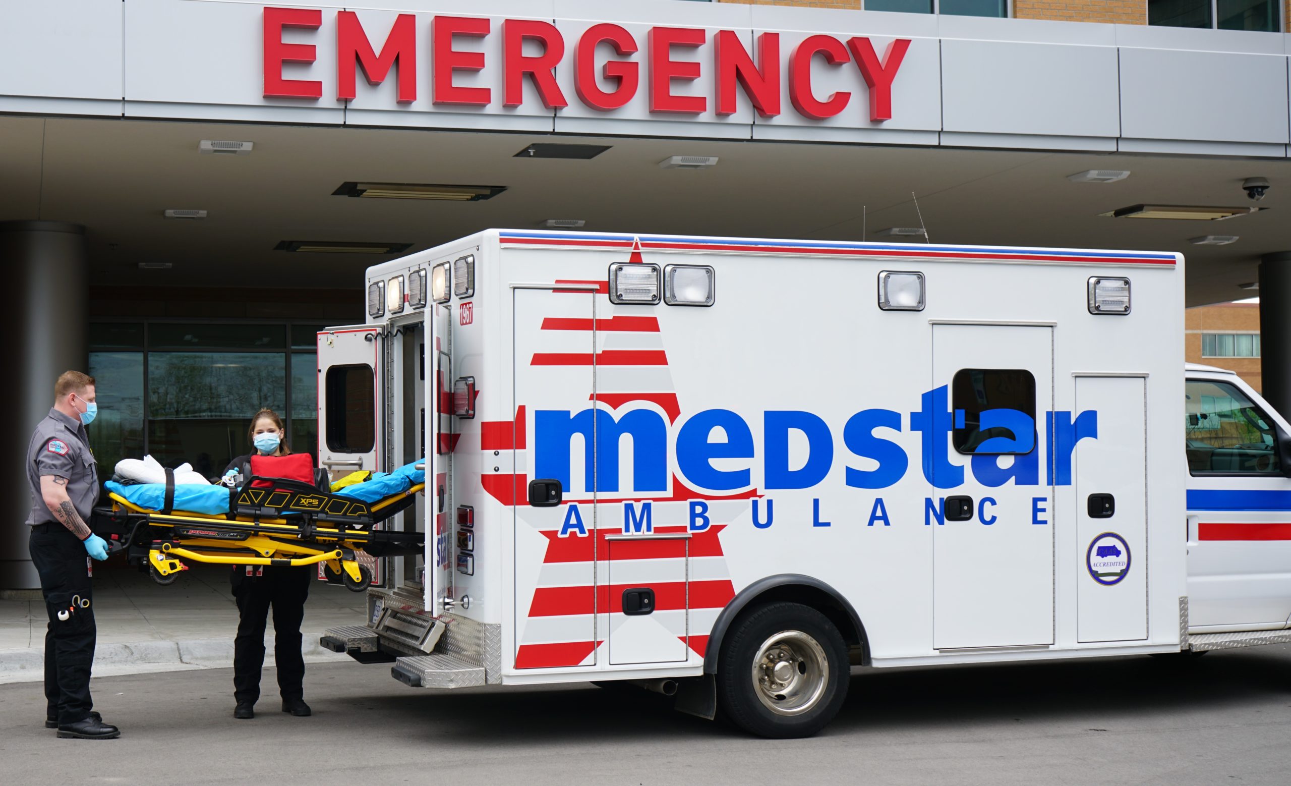 emt and paramedic with stretcher and ambulance outside of a emergency department